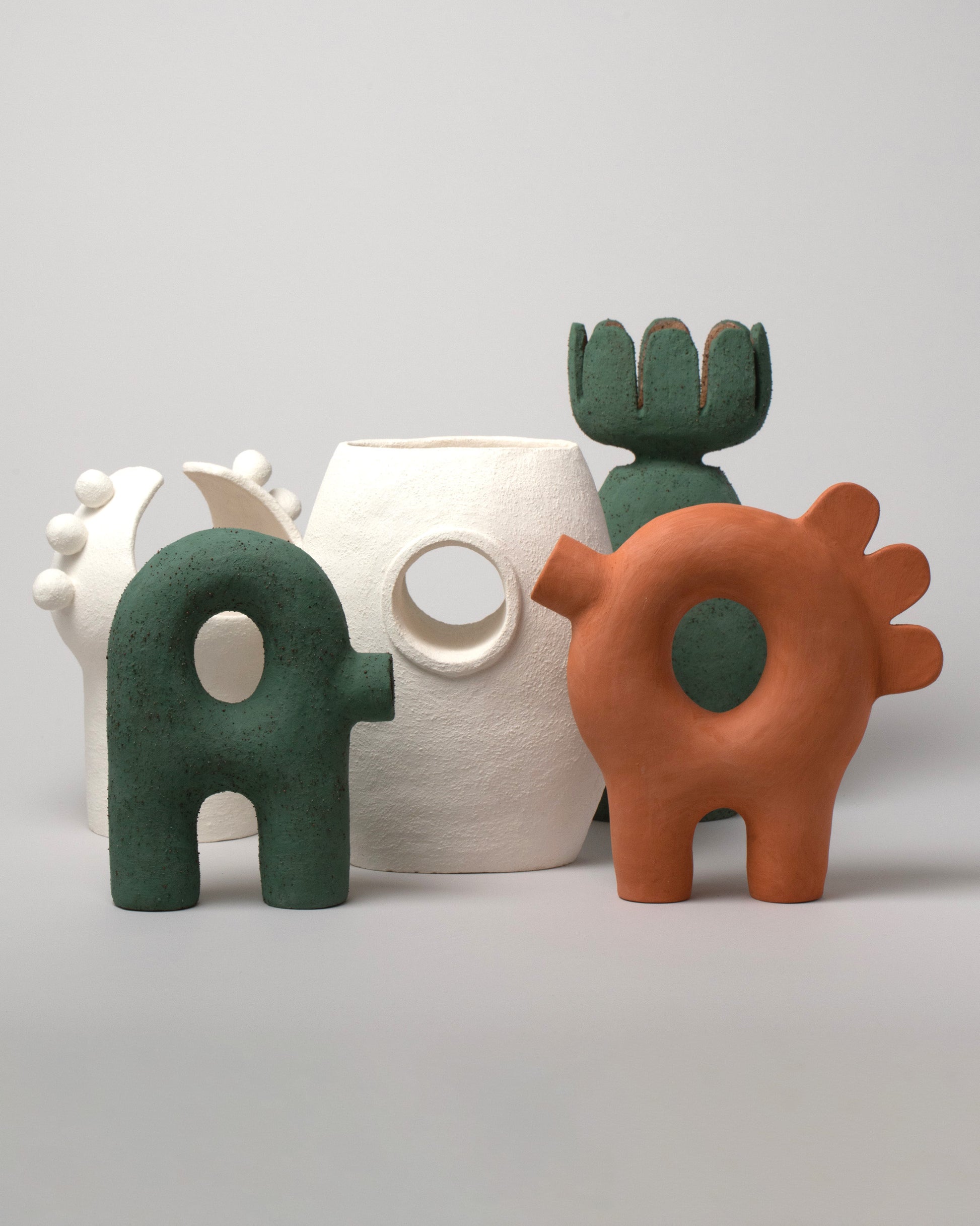 Group photo of Stephanie Phillips Curvature Sculpture, Ferdi Sculpture, Flower Sculpture, Moon Bulb Sculpture, and Single Barrel Vessel on light color background.