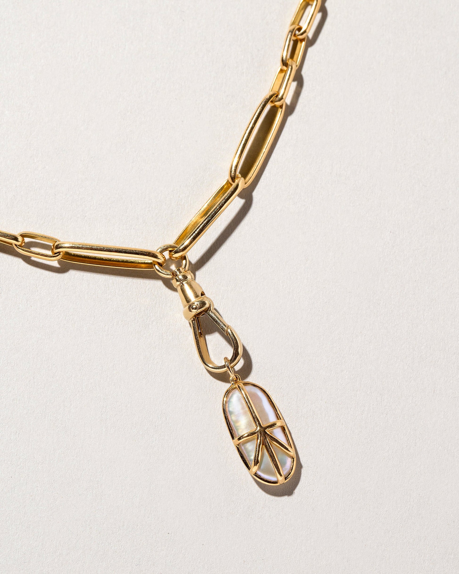 Closeup details of the Grand Swivel Fob paired with the Long Loop Chain Necklace and charm on light color background.