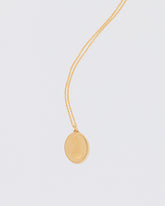 Finished Large Oval Memento Necklace engraved with an abstract symbol on light color background.