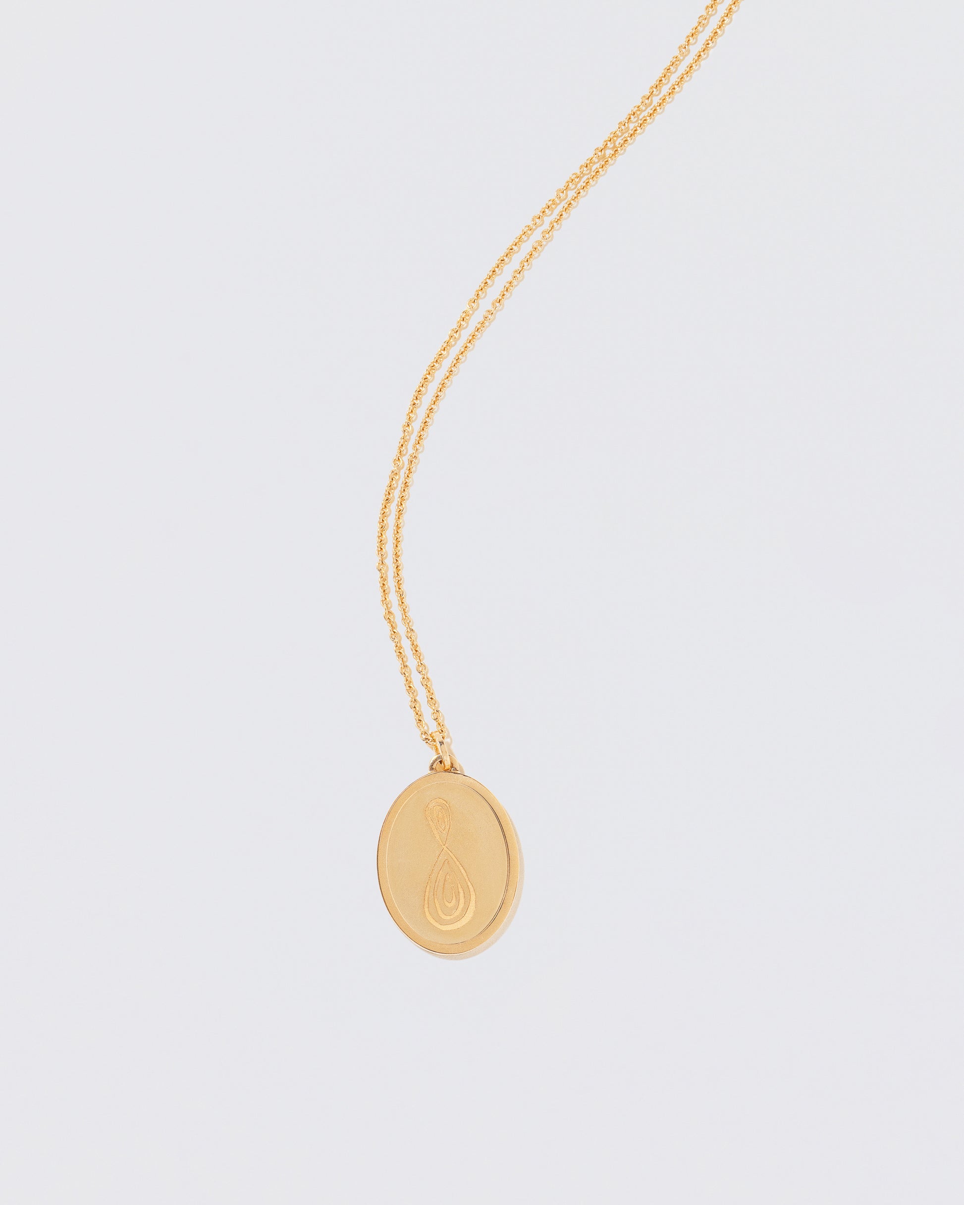 Finished Large Oval Memento Necklace engraved with an abstract symbol on light color background.