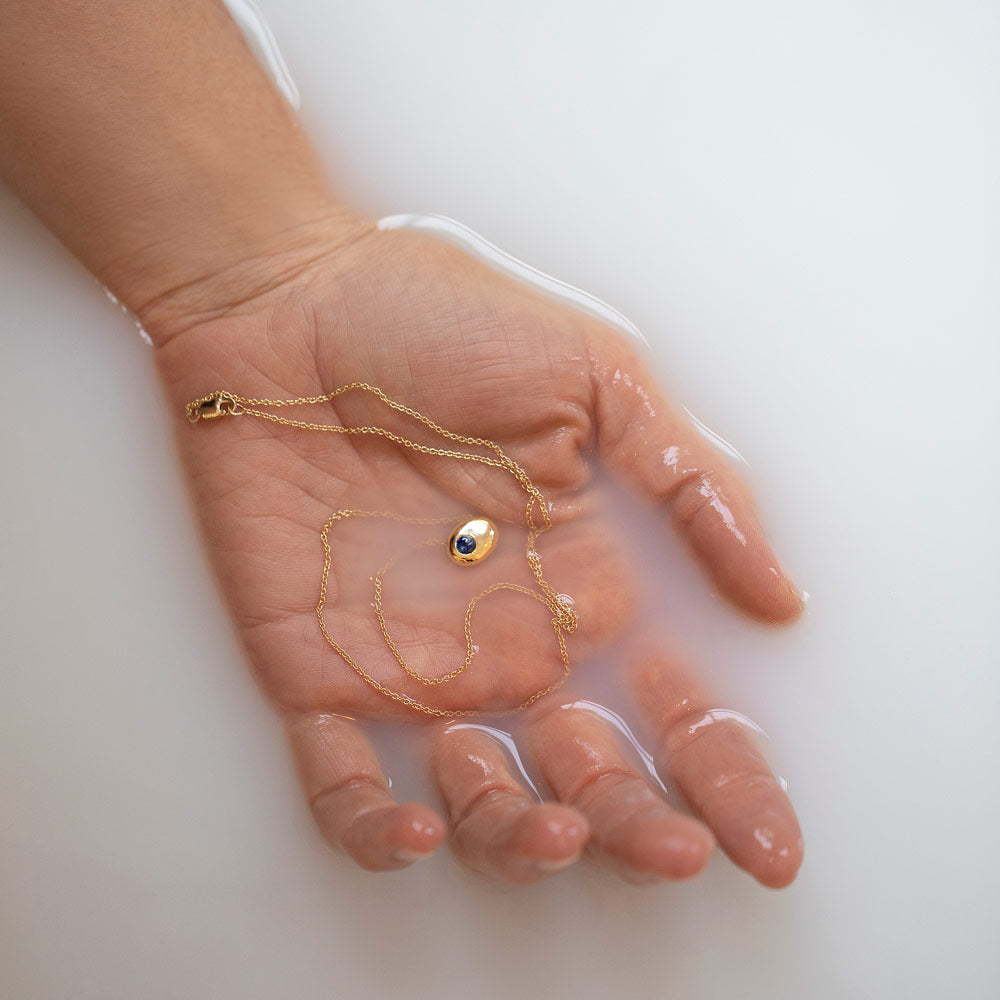 product_details::Styled image of the Gold Bicolor Blue Sapphire Level Necklace in hand.