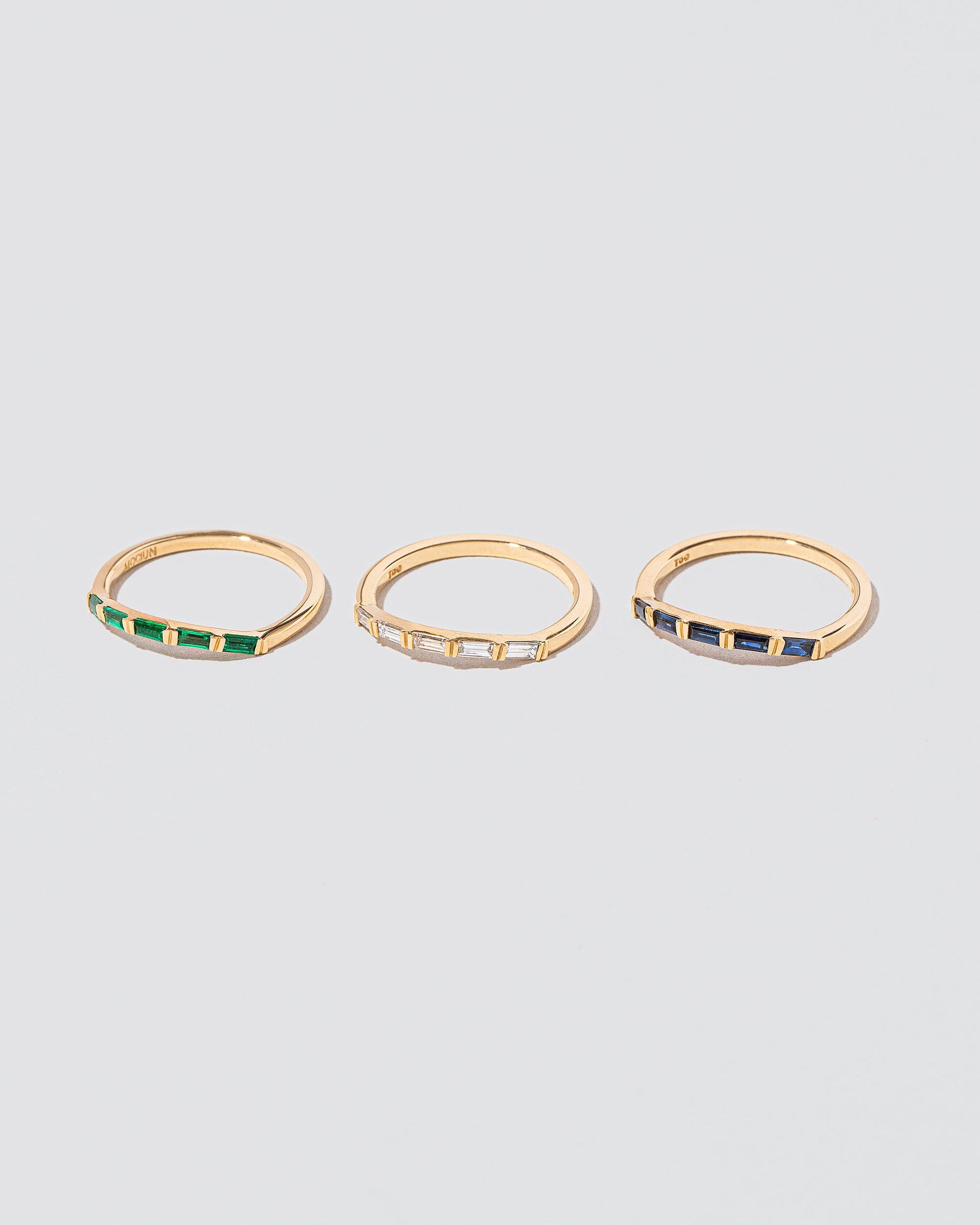 Closeup detail of a group of Emerald, White Diamond and SapphireSapphire Bow Bands on light color background.